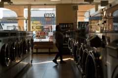 12/11/19 – LONG BEACH, CALIF: Diana Sandoval inspects the tops of the washers as she tidies up around the Anaheim and Redondo Laundromat. She's worked here for three years. Photograph by Dillon Hulse.